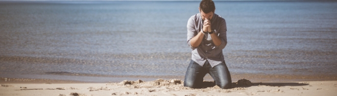 Hombre de rodillas orando en la playa